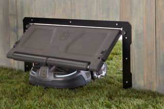 Robotic lawn mower entering a wooden enclosure through a hinged door.