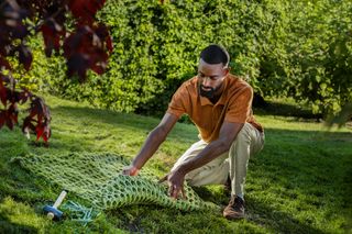 A person laying down a green net on a grassy area in a garden.