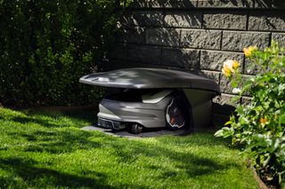 Husqvarna Automower®Garage. Robotic lawn mower parked in a robotic mower house in a garden near a stone wall.