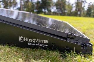 Nahaufnahme eines Husqvarna Solarladegeräts auf Rasen in einer Gartenumgebung.