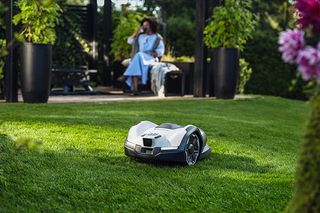 Robotgrasmaaier die in een tuin werkt met een persoon op de achtergrond.