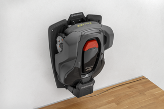 Husqvarna robotic lawn mower mounted on a wall for storage.