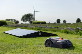 Robotic lawn mower charged by solar panels, operating on a semi-rough at a golf course.