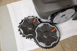Close-up of a robotic lawn mower with two spare wheels on a towel.