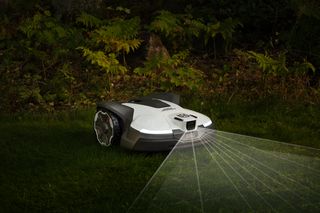 Un robot tondeuse fonctionnant la nuit avec des phares éclairant l’allée dans un jardin.