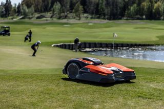 ゴルファーを背景に、池の近くのゴルフコースで稼働するロボット芝刈り機。