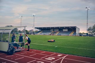 Un robot tondeuse fonctionnant sur un terrain de sport près d’une piste de course, avec un stade en arrière-plan.