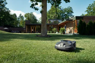 Robot cortacésped funcionando en un jardín con una casa moderna al fondo.