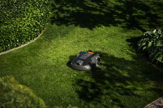 A robotic lawn mower operating on a well-maintained lawn with surrounding greenery.