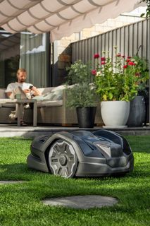 Robotic lawn mower operating on a well-maintained lawn in a garden setting.