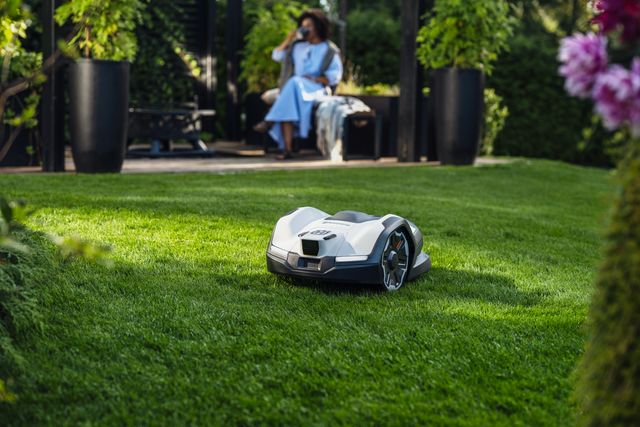 A robotic lawn mower operating on a well-maintained lawn with a person sitting in the background.