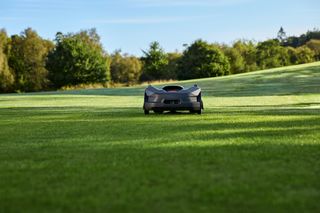 Robot tondeuse fonctionnant sur un grand champ herbeux avec des arbres en arrière-plan.