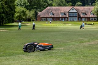 Robot tondeuse fonctionnant sur un parcours de golf avec des golfeurs en arrière-plan.