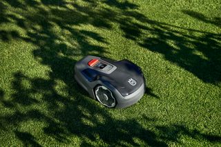 Robotgräsklippare på en välskött gräsmatta med skuggor av träd.
