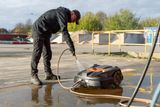 A person cleaning a robotic lawn mower with a hose in an outdoor setting.