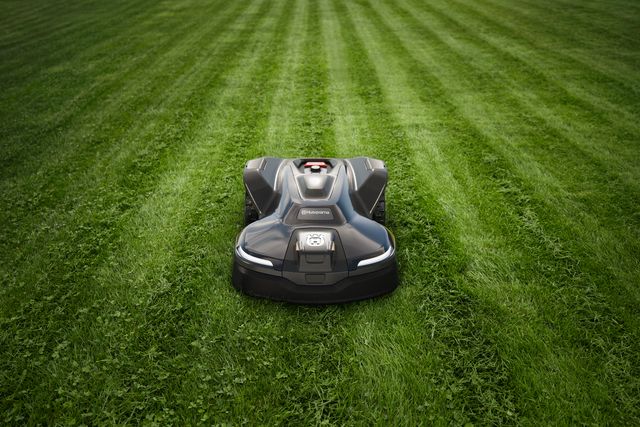 Husqvarna robotic lawn mower cutting grass on a large lawn with visible mowing stripes.