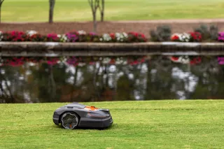Robotic lawn mower operating on a grassy area near a reflective pond.