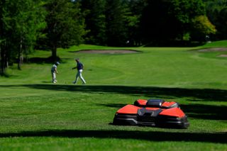 2 人のゴルファーを背景にしたゴルフのフェアウェイ上のロボット芝刈機。