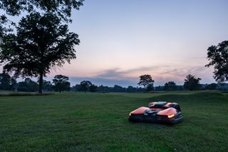 Tondeuse à gazon robotisée fonctionnant sur un grand champ gazonné au crépuscule.