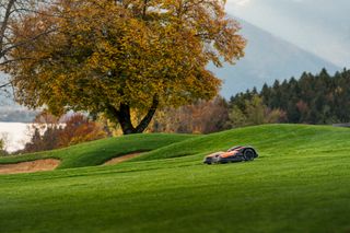 Robot tondeuse fonctionnant sur une pente herbeuse avec des arbres d’automne en arrière-plan.