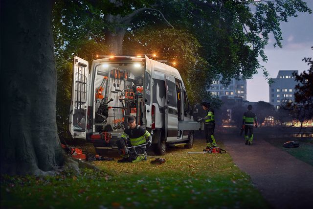 Arbeiter organisieren Werkzeuge in einem Lieferwagen, der in der Dämmerung in einem Park geparkt ist.