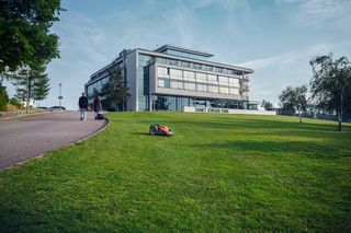 A robotic lawn mower operating on a grassy slope in front of a modern building.
