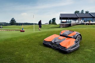 Ein Mähroboter, der auf einem Golfplatz betrieben wird, während eine Person in der Nähe spazieren geht.