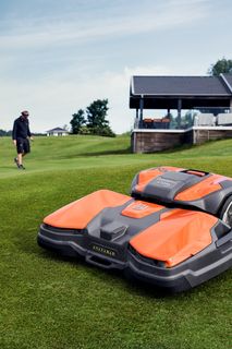 ゴルフ場で歩いているロボット芝刈り機で、近くを歩いている人。