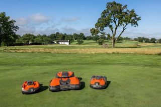 Three robotic lawn mowers on a grassy field with a scenic background.