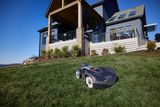 Robotic lawn mower operating in a garden in front of a modern house.