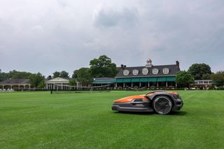 Robotic lawn mower operating on a large lawn in front of a grand house.