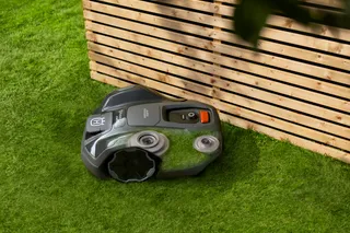 Mähroboter, der in der Nähe eines Holzzauns in einem Garten arbeitet.
