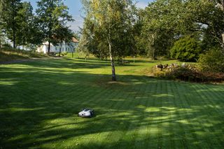 Robotic lawn mower operating in a garden with a satellite signal icon overlay.