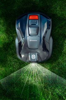 Robotyczna kosiarka pracująca na trawie z widocznym cyfrowym wyświetlaczem i przyciskiem stop.