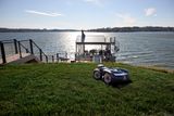 Robotic lawn mower operating on grass near a lakeside dock.