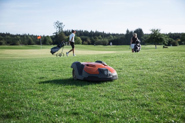 A robotic lawn mower operating on a golf course with people in the background.