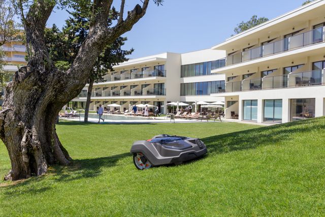 Robotic lawn mower operating on a grassy slope near a modern hotel building.