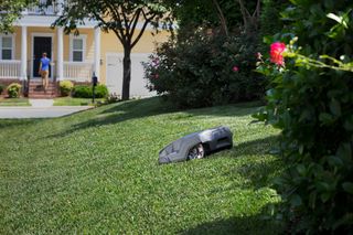 A robotic lawn mower operating on a grassy slope in a residential garden.