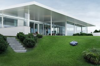 Ein Mähroboter auf einer Wiese vor einem modernen Haus.