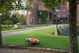 Robotic lawn mower operating on a manicured lawn in front of a historic building.