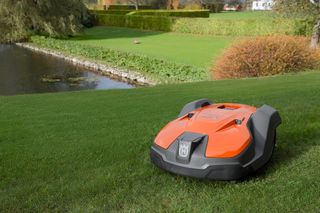 Tondeuse à gazon robotisée fonctionnant sur une pelouse gazonnée près d’un étang.