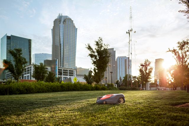 Robotic lawn mower operating on a grassy area with a city skyline in the background.