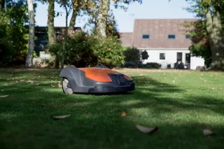 Robô corta-relva a funcionar num jardim com uma casa ao fundo.