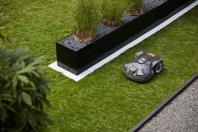 Robotgräsklippare som arbetar i en trädgård nära en dekorativ kruka.