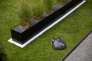 Robotic lawn mower operating on a neatly manicured lawn beside a modern planter.
