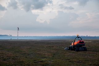 En åkgräsklippare som arbetar på ett stort gräsbevuxet fält med molnig himmel.