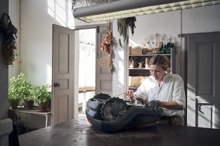 Una persona trabajando en un robot cortacésped en un taller, rodeada de plantas y herramientas.