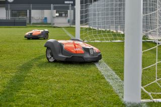 Robotic lawn mowers operating on a football field, one near a goal post.
