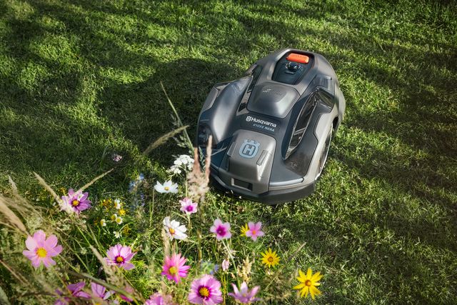 Robotska kosilica koja radi na travnatom travnjaku sa šarenim cvjetovima u prvom planu.