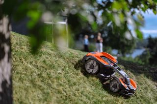 背景がぼやけた草が茂った斜面で動作するロボット芝刈り機。